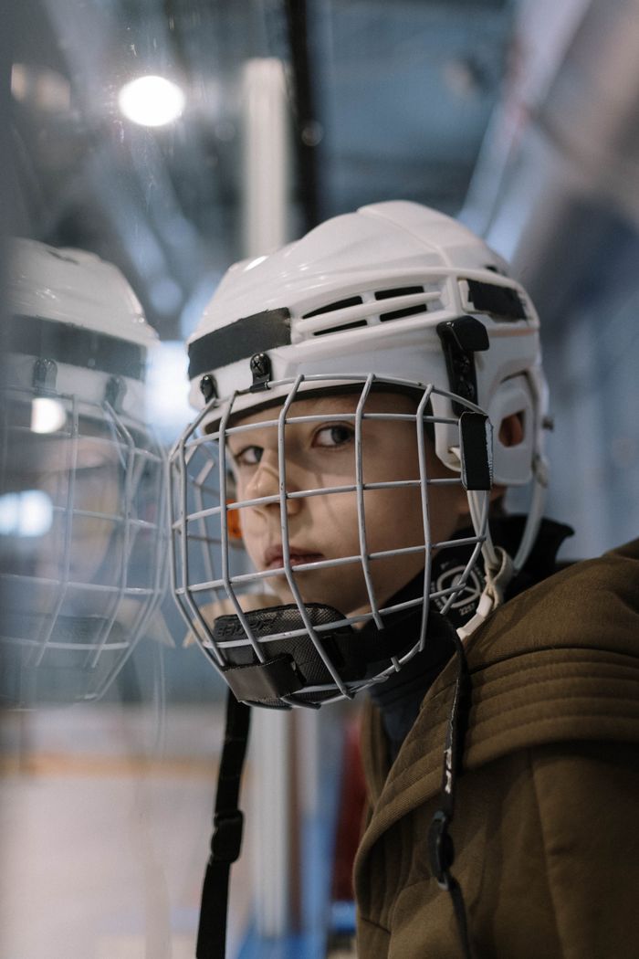 Close-up portrait of a young ice hockey player wearing protective gear and helmet indoors.