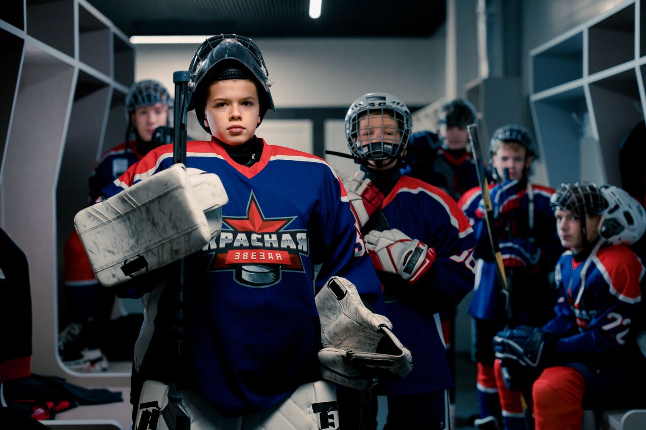 Young ice hockey team in locker room preparing for game, wearing full gear.