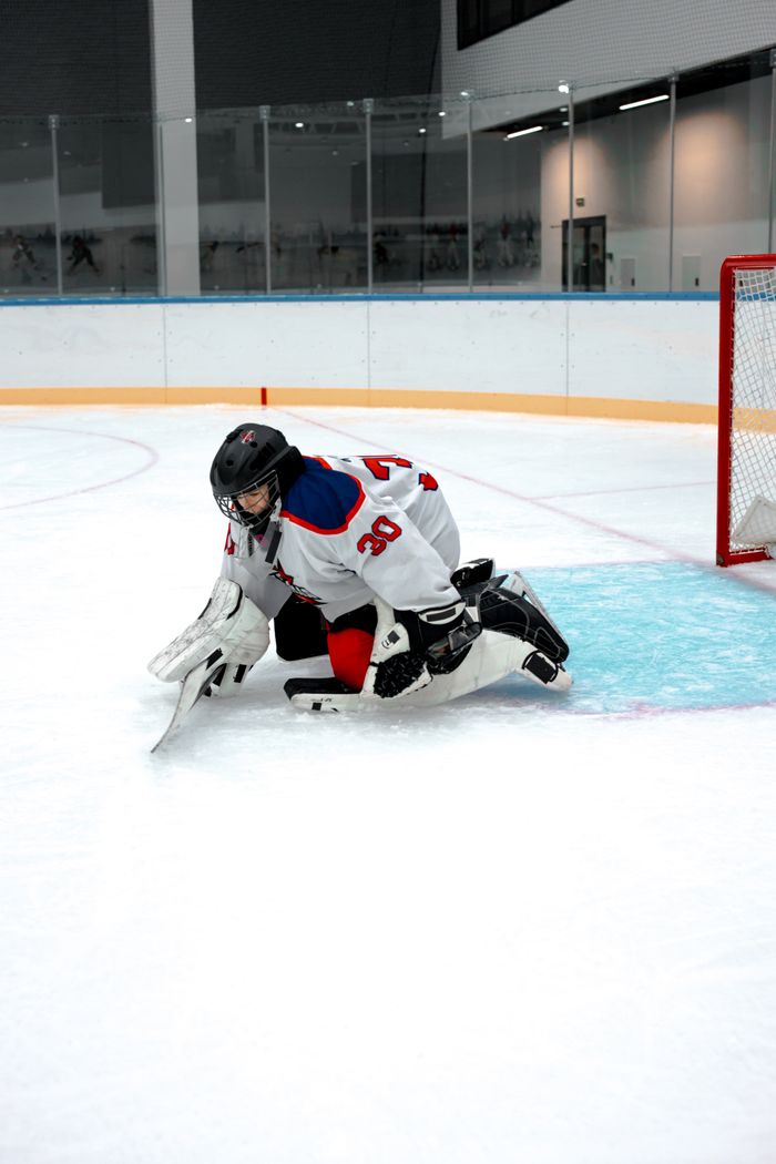 Ice hockey goalie in action during a game at an indoor rink.